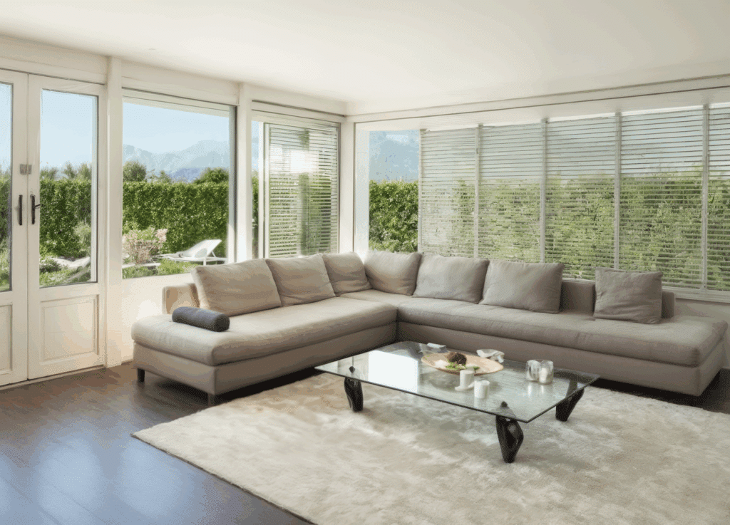 Salón luminoso con sofá en L y grandes ventanas a medida de Sabaya en PVC blanco con vistas al jardín